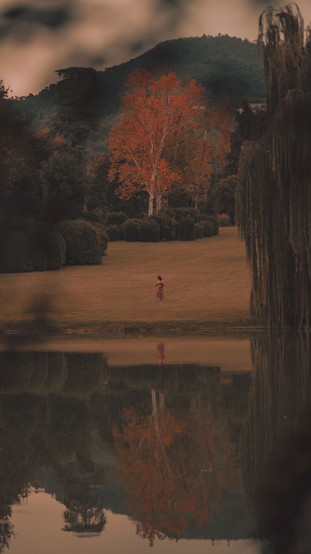 Figura in un parco riflessa in un lago
